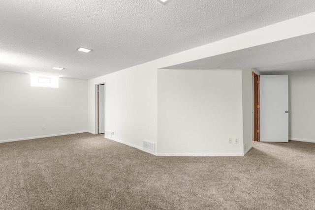 spare room featuring carpet, visible vents, a textured ceiling, and baseboards