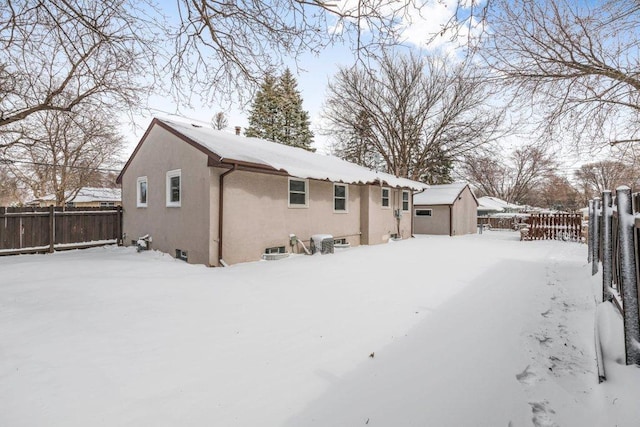 snow covered house with an outbuilding, fence, and stucco siding