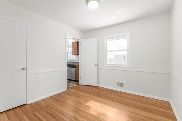 unfurnished bedroom with light wood-style floors, visible vents, connected bathroom, and baseboards