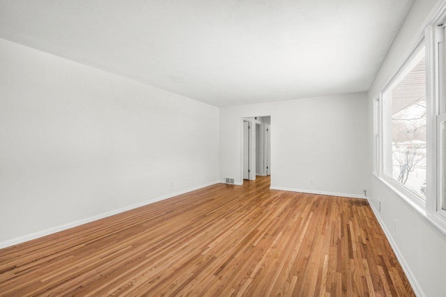 spare room with light wood-style floors, visible vents, and baseboards