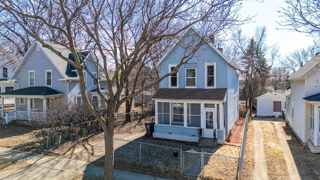 traditional-style house featuring dirt driveway, a fenced front yard, entry steps, roof with shingles, and a sunroom