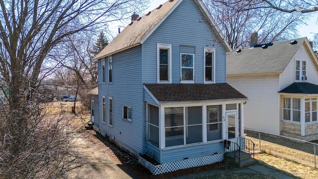 view of side of home featuring entry steps, fence, roof with shingles, and a sunroom