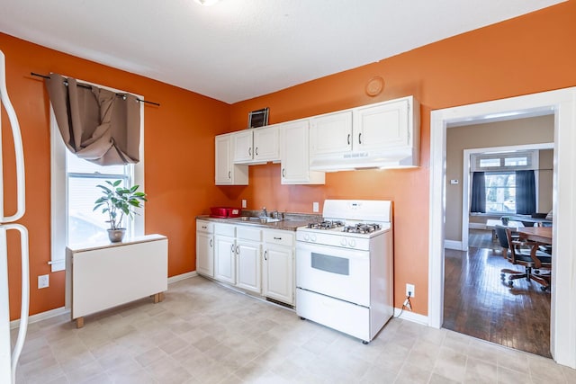 kitchen featuring white gas stove, white cabinetry, under cabinet range hood, and a sink