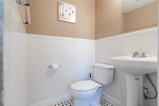 half bath featuring toilet, tile walls, wainscoting, and tile patterned flooring