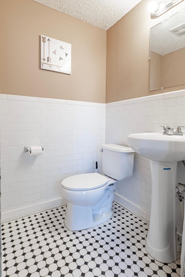 bathroom featuring visible vents, a wainscoted wall, a textured ceiling, tile walls, and toilet