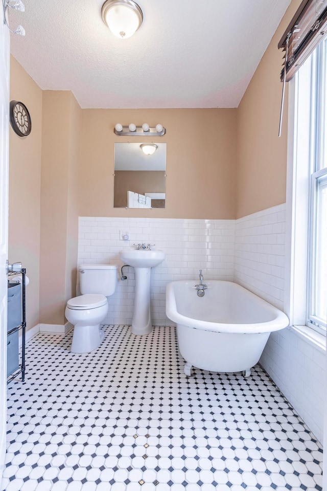 full bath with toilet, a freestanding bath, tile walls, and a sink