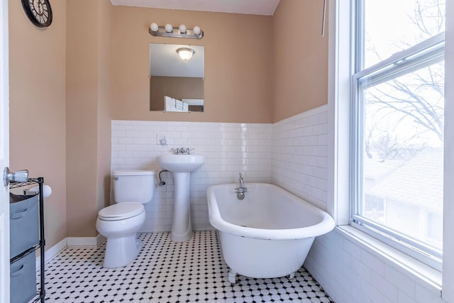 full bath with tile walls, a freestanding tub, toilet, and a wealth of natural light