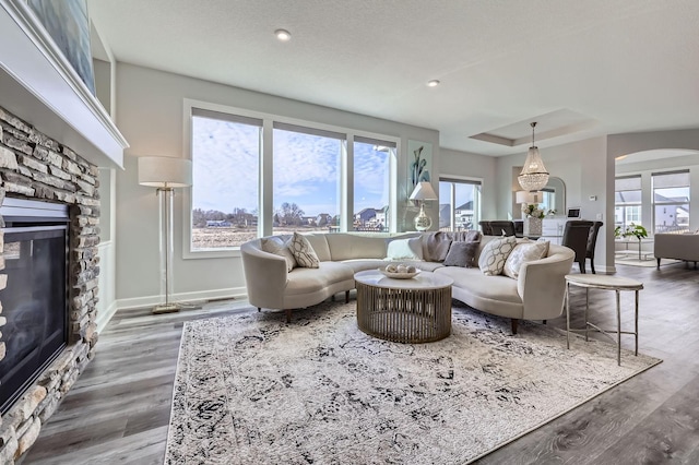 living area with arched walkways, a stone fireplace, wood finished floors, and baseboards