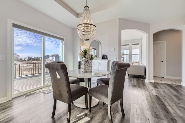 dining area with a tray ceiling, wood finished floors, visible vents, and baseboards