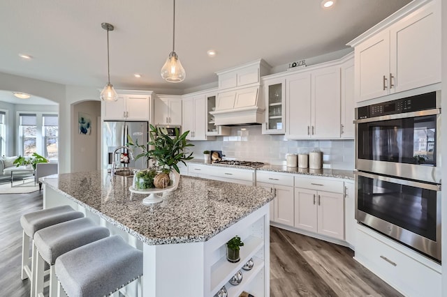 kitchen featuring arched walkways, tasteful backsplash, appliances with stainless steel finishes, white cabinetry, and wood finished floors