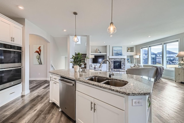 kitchen featuring appliances with stainless steel finishes, open floor plan, dark wood-style flooring, a stone fireplace, and a sink