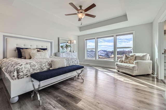 bedroom with a tray ceiling, wood finished floors, a ceiling fan, and baseboards