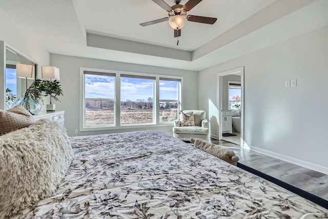 bedroom featuring a tray ceiling, wood finished floors, a ceiling fan, and baseboards