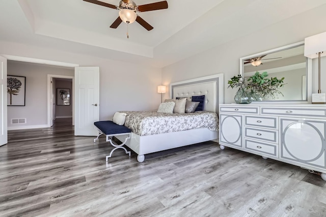 bedroom featuring wood finished floors, a raised ceiling, visible vents, and a ceiling fan