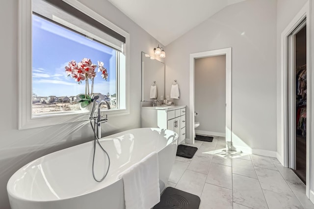 bathroom with baseboards, lofted ceiling, toilet, vanity, and a freestanding tub