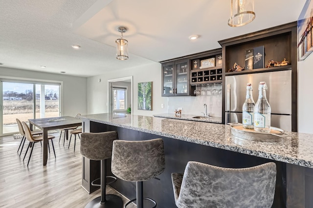 kitchen featuring light wood-type flooring, hanging light fixtures, a sink, and freestanding refrigerator