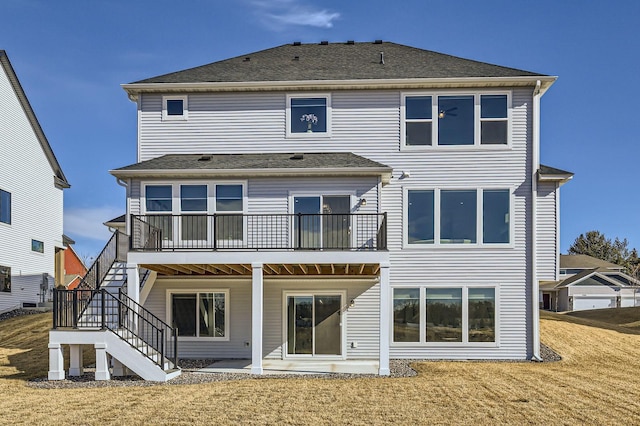 rear view of house featuring roof with shingles, a patio area, a lawn, and stairs