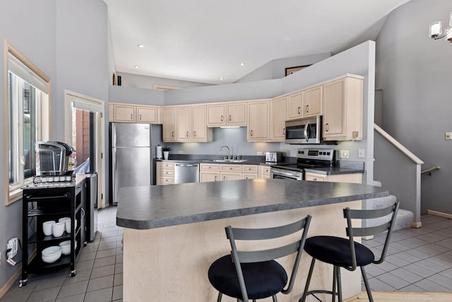 kitchen featuring dark countertops, light brown cabinets, stainless steel appliances, and a sink