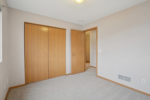 unfurnished bedroom with baseboards, visible vents, a closet, and light colored carpet