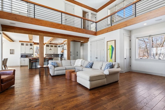 living room featuring dark wood-type flooring, a towering ceiling, and baseboards