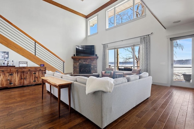 living area featuring baseboards, stairway, dark wood-type flooring, a high ceiling, and a stone fireplace