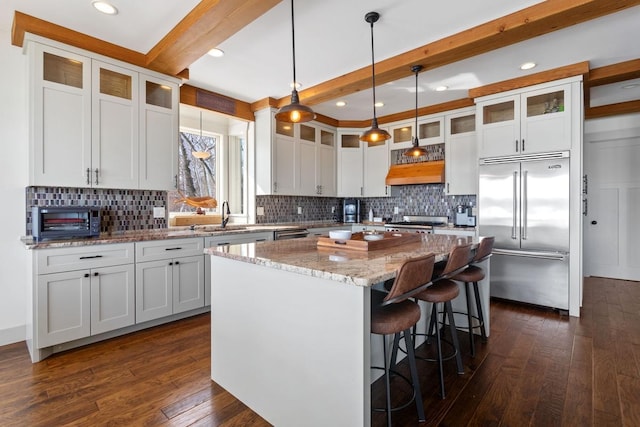 kitchen featuring dark wood finished floors, a kitchen island, beamed ceiling, stainless steel appliances, and a sink