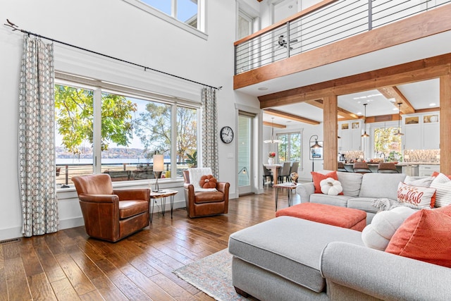 living room with hardwood / wood-style flooring, visible vents, a towering ceiling, baseboards, and beamed ceiling