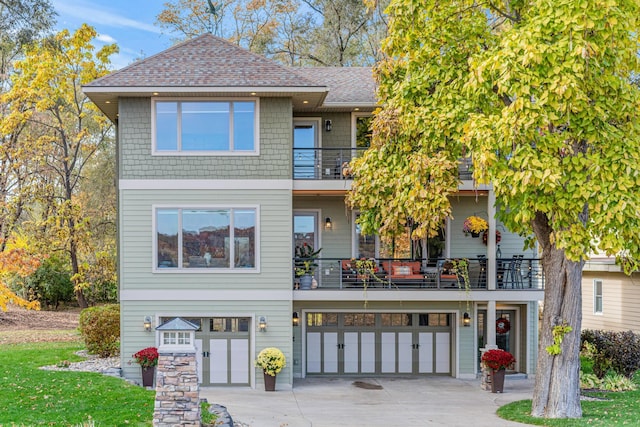 view of front of home featuring a garage, driveway, a balcony, and a shingled roof