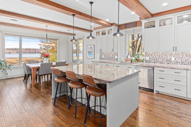 kitchen featuring white cabinets, dishwasher, a sink, beamed ceiling, and a center island