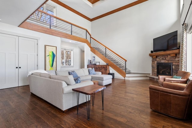 living room with a stone fireplace, dark wood finished floors, stairs, and a towering ceiling