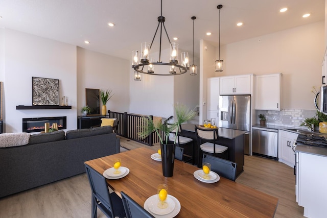 dining room with recessed lighting, a glass covered fireplace, light wood-style flooring, and a high ceiling