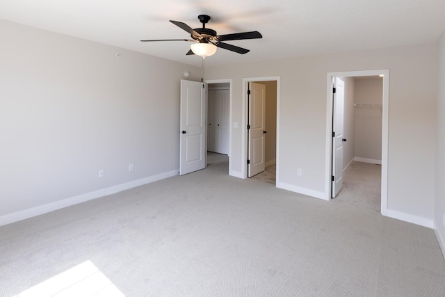 unfurnished bedroom featuring a walk in closet, a ceiling fan, a closet, baseboards, and light colored carpet