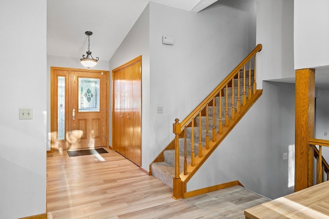 foyer with vaulted ceiling, wood finished floors, stairs, and baseboards