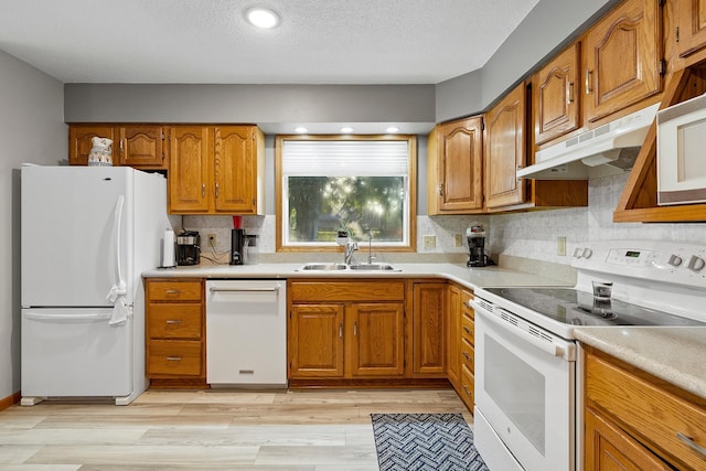 kitchen featuring white appliances, brown cabinets, light countertops, under cabinet range hood, and a sink