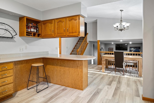 kitchen with brown cabinetry, light wood-type flooring, light countertops, and a notable chandelier