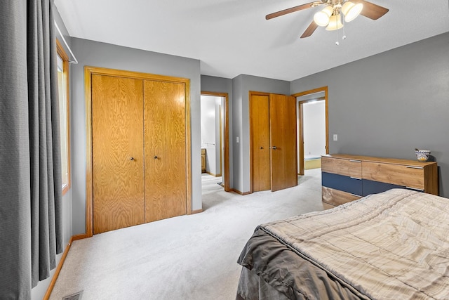 bedroom with light carpet, ceiling fan, baseboards, and two closets