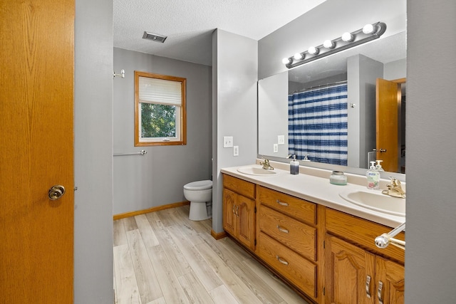 bathroom with toilet, a textured ceiling, a sink, and wood finished floors