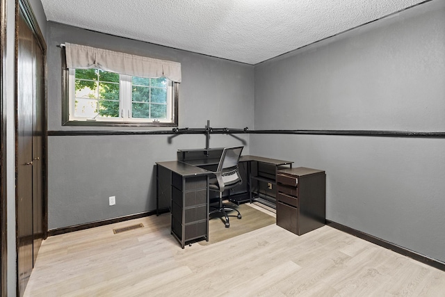 home office featuring a textured ceiling, light wood-type flooring, visible vents, and baseboards