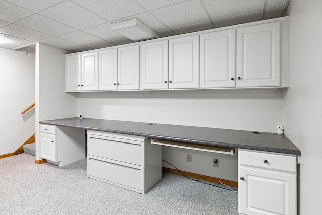 unfurnished office featuring a drop ceiling, built in study area, light colored carpet, and baseboards