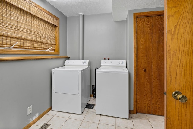 clothes washing area featuring light tile patterned floors, a textured ceiling, laundry area, independent washer and dryer, and baseboards