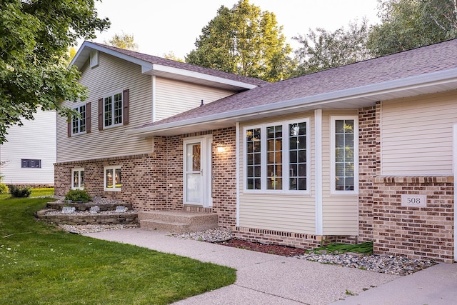 view of front of home featuring roof with shingles, brick siding, and a front lawn