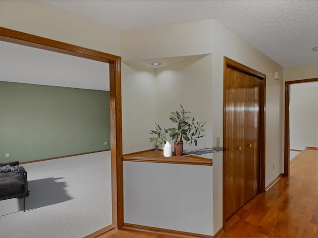 hall with a textured ceiling, wood finished floors, and baseboards