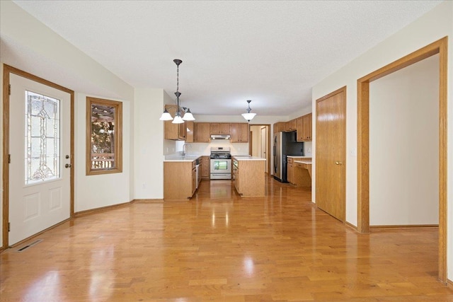 kitchen with stainless steel appliances, light countertops, visible vents, brown cabinetry, and light wood-type flooring