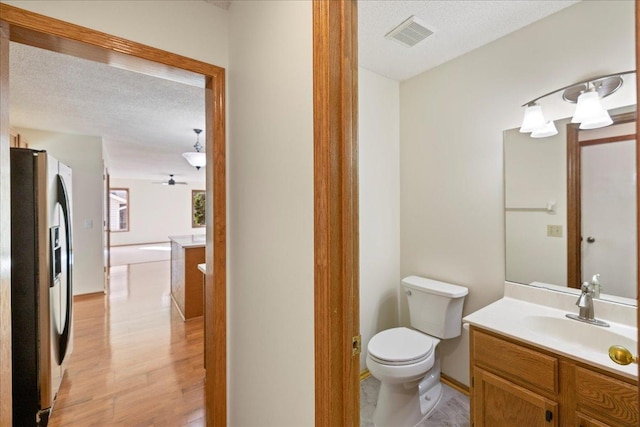 half bath with visible vents, toilet, a textured ceiling, vanity, and wood finished floors