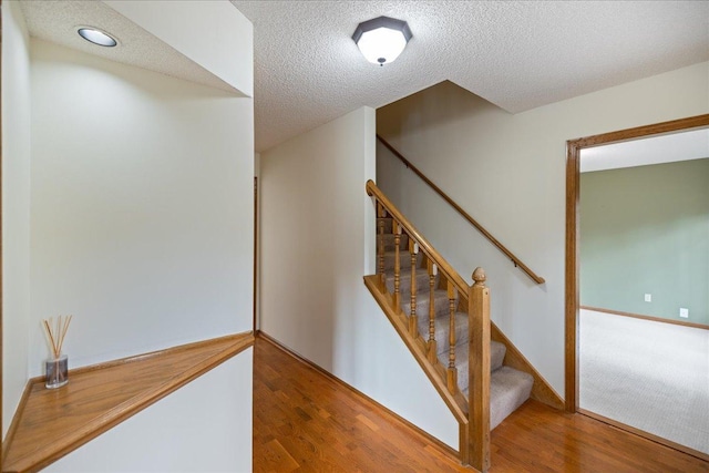 stairway with a textured ceiling, wood finished floors, and baseboards