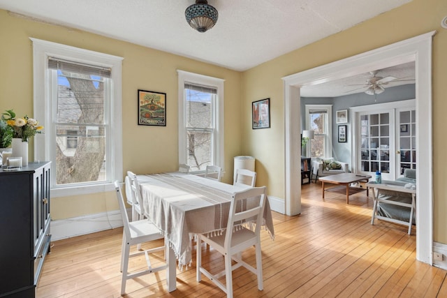 dining room featuring light wood-style floors, ceiling fan, baseboards, and a textured ceiling