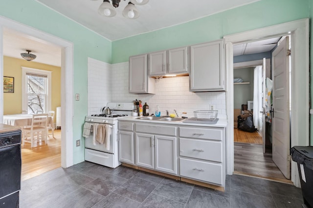 kitchen with black dishwasher, white gas range, light countertops, backsplash, and a sink