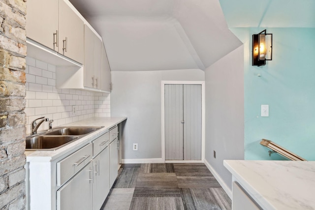 kitchen featuring tasteful backsplash, baseboards, vaulted ceiling, light countertops, and a sink