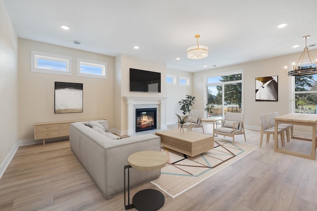 living area with light wood finished floors, baseboards, a high end fireplace, an inviting chandelier, and recessed lighting