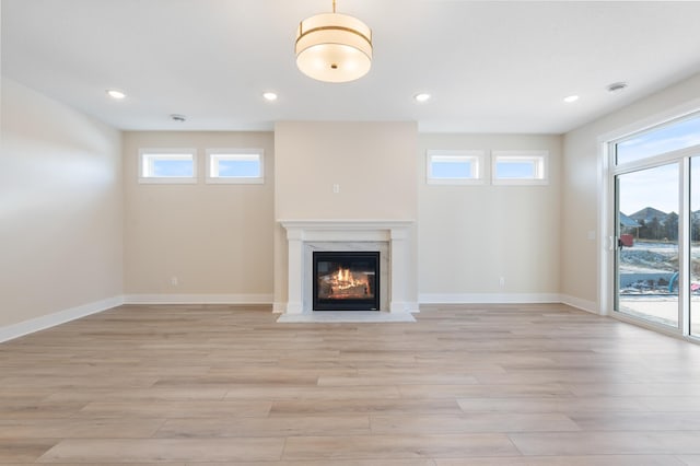 unfurnished living room featuring baseboards, recessed lighting, a fireplace, and light wood-style floors